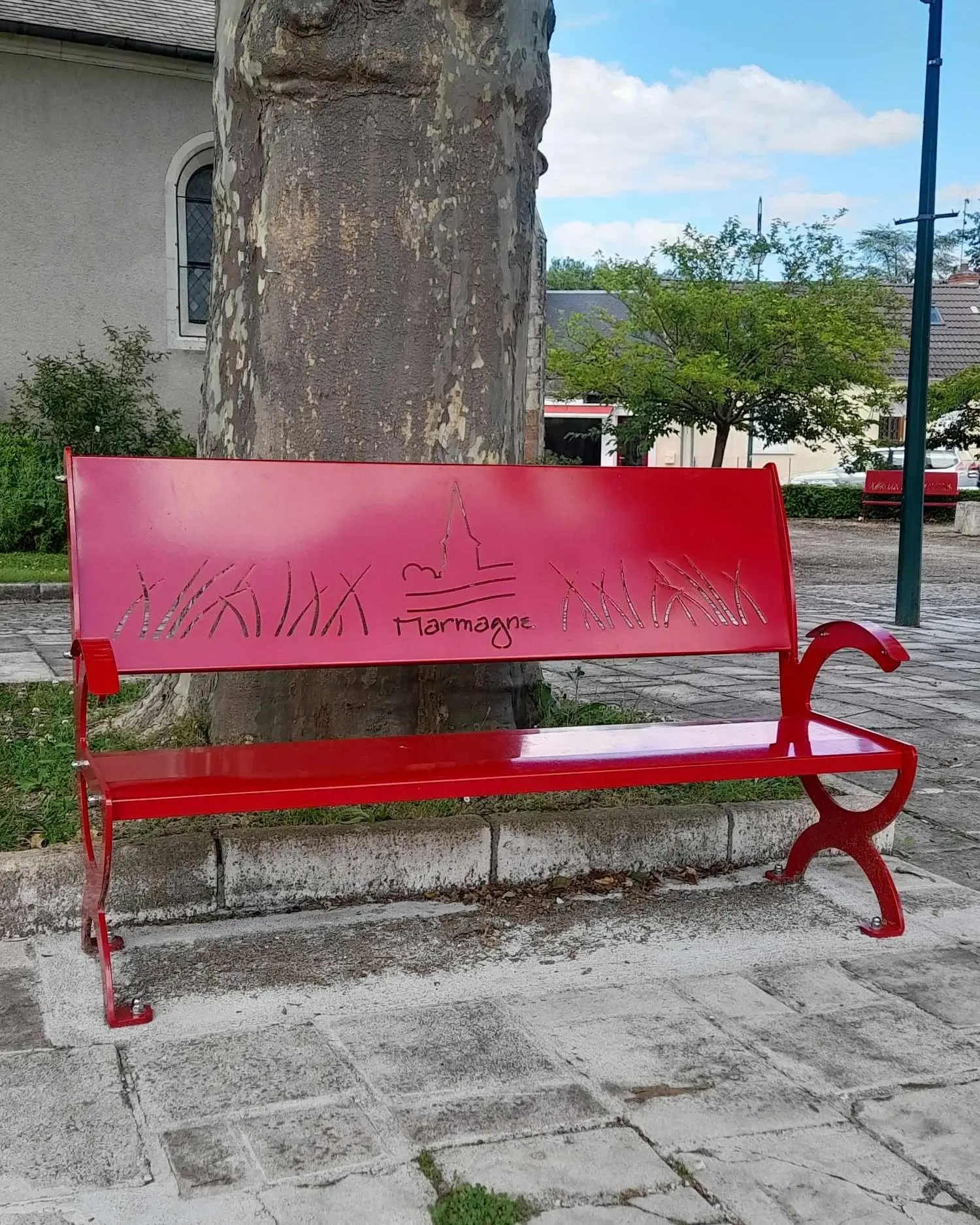 Banc public en acier rouge personnalisé pour Marmagne, avec le nom de la commune et la silhouette du clocher découpés dans le dossier