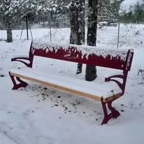 Banc public métallique rouge avec assise en bois, photographié sous la neige sur un espace communal