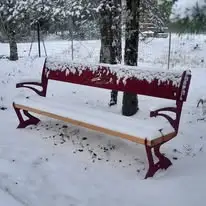Banc public rouge à lames de bois photographié sous la neige, illustrant le confort de l’assise bois en hiver