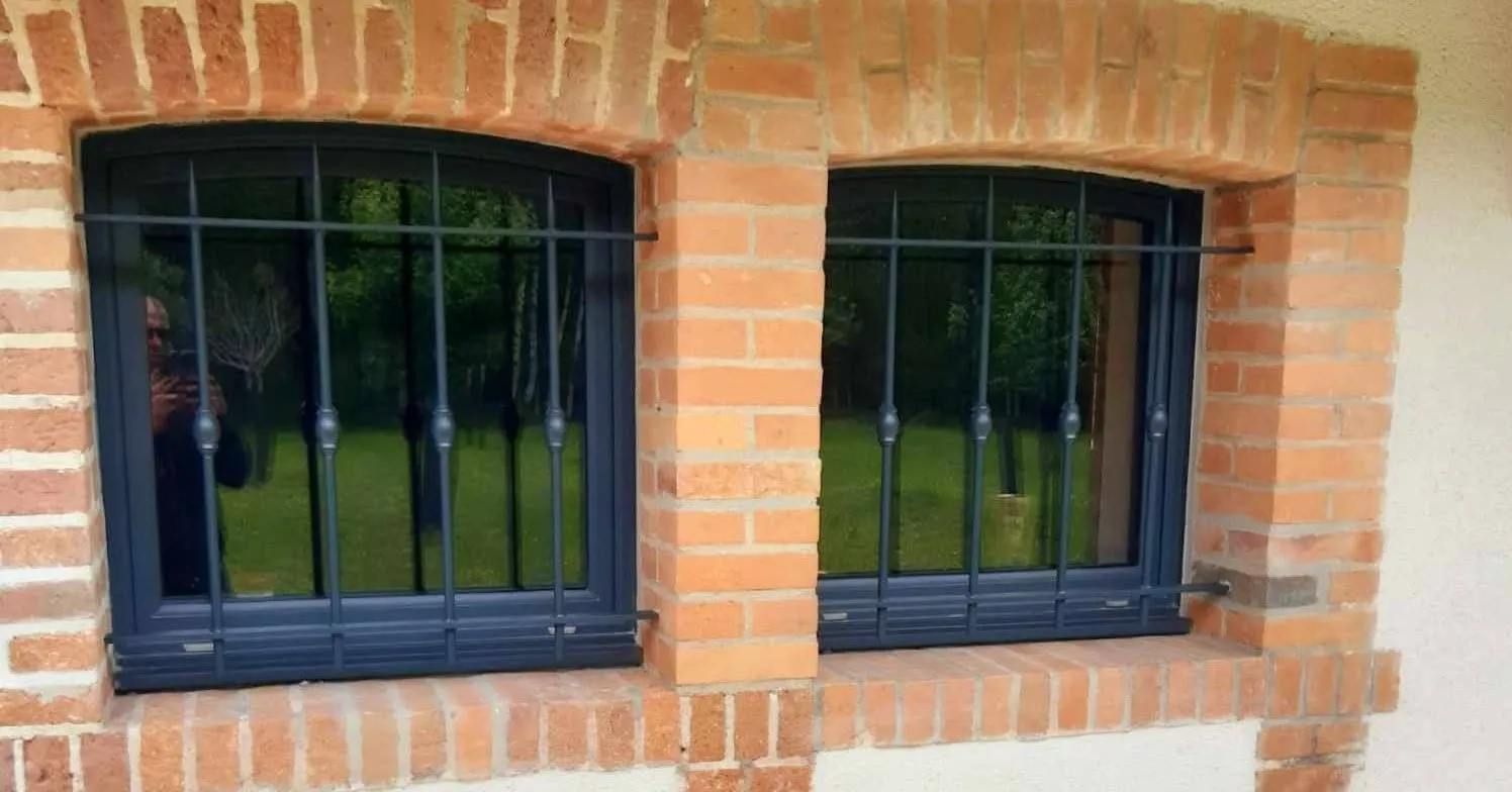 Grilles métalliques noires installées devant deux fenêtres cintrées