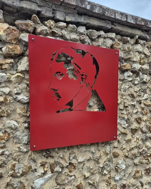 Portrait découpé dans une plaque d’acier rouge fixée sur un mur en pierre