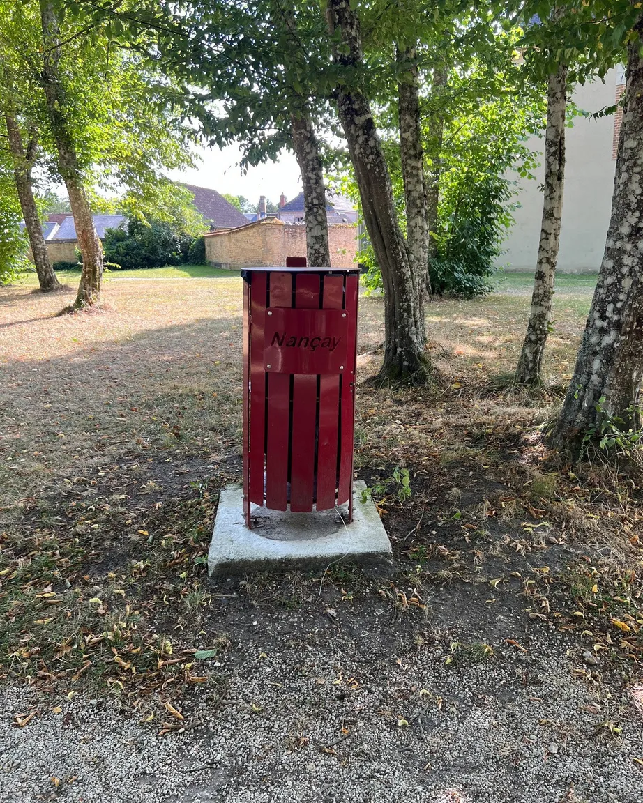 Corbeille urbaine rouge personnalisée au nom de Nançay, installée sur un massif béton dans un parc