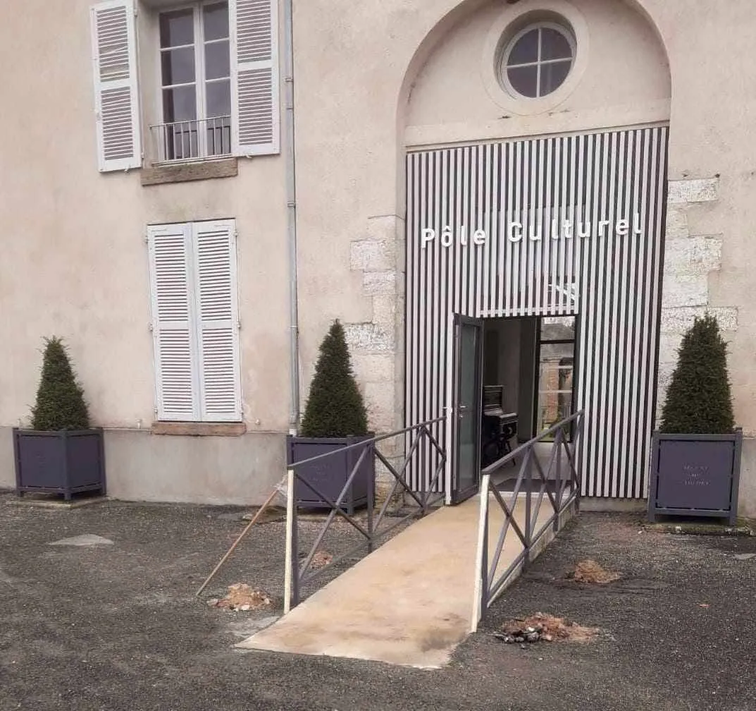 Rampe d'accès et garde-corps métalliques posés devant l'entrée d'un pôle culturel
